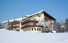 Ramswirt, © Ramswirt, Familie Pichler Ein großes, traditionelles Gebäude im Schnee mit Holzverzierungen und einem verschneiten Baum davor.