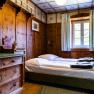 Doppelzimmer, © Katrin Nusterer Rustikales Doppelzimmer mit Holzwänden, einem Bett und einer Kommode.