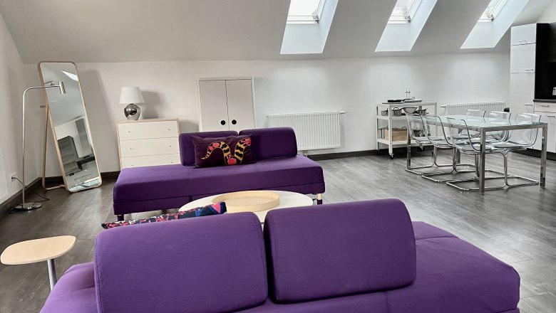 Loft am Hauptplatz, © Relax Apartments Modernes Loft mit lila Sofas, Esstisch und Dachfenstern.