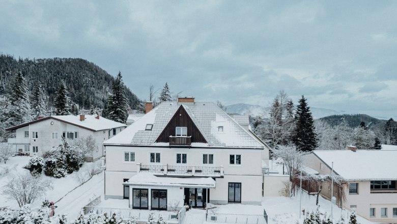 Der Löffler, © Nicole Seiser Ein großes, schneebedecktes Haus in einer winterlichen Landschaft mit Bergen im Hintergrund.