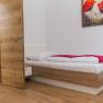 Zimmer, © Familie Gschaider Ein einfach eingerichtetes Zimmer mit einem Einzelbett, Holzboden und einem Bild mit roten Blumen an der Wand.