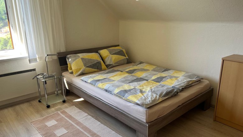 Ferienwohnungen Riedl, © Familie Riedl Ein gemütliches Schlafzimmer mit einem Doppelbett, gemusterten Bettbezügen, einem kleinen Nachttisch und einem Fenster mit Vorhängen.