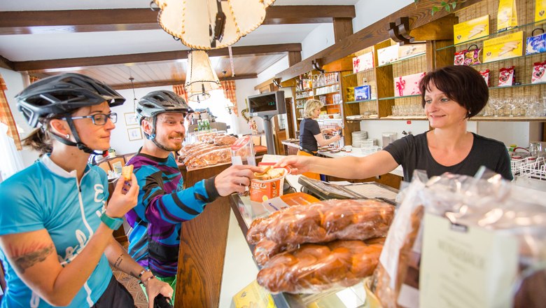 Café Konditorei Alber direkt an der Schwarzatal Radroute, © NÖW - Kikinder Zwei Radfahrer in einem Café, die von einer Verkäuferin bedient werden.