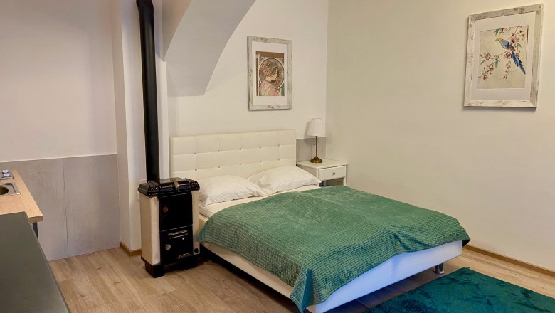 Zemlinsky Hof, © Wiener Alpen Ein gemütliches Schlafzimmer mit einem weißen Bett, grüner Decke, Teppich und zwei Bildern an der Wand.