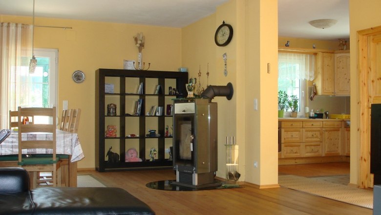 Wohnküche, © Vadim Drozdov Wohnküche mit Holzmöbeln, Esstisch, Regal, Kamin und offener Küche.