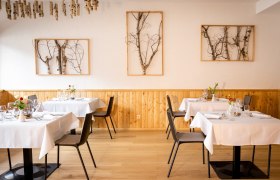 Parkhotel Hirschwang, Restaurant Raxblick, © Friedl und Schmatz Elegantes Restaurant mit Holzwänden, weißen Tischdecken und Birkenkunst an den Wänden.