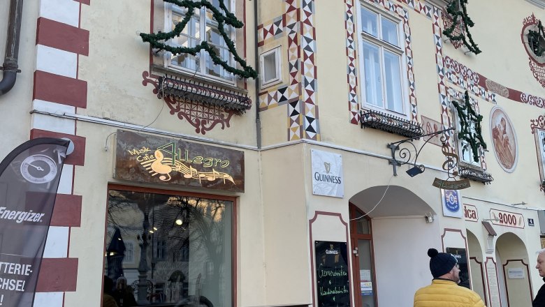 Cafe Allegro, © Wiener Alpen/Lechner Außenansicht des Cafe Allegro mit dekorierter Fassade und zwei Personen im Gespräch.