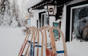 Enzianhütte, © Nixxipixx Fotografie & Design e.U. Nicole Seiser Verschneite Hütte mit Schlitten davor.