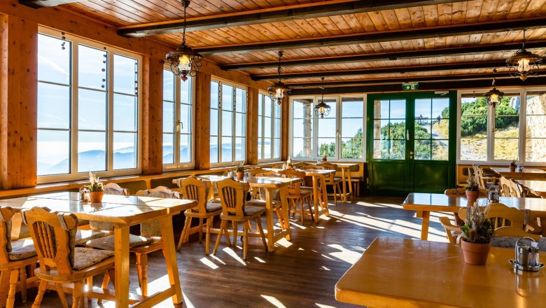 Gaststube, © Katrin Nusterer Gemütliche Gaststube mit Holzmöbeln und großen Fenstern, die einen Blick auf die Berge bieten.