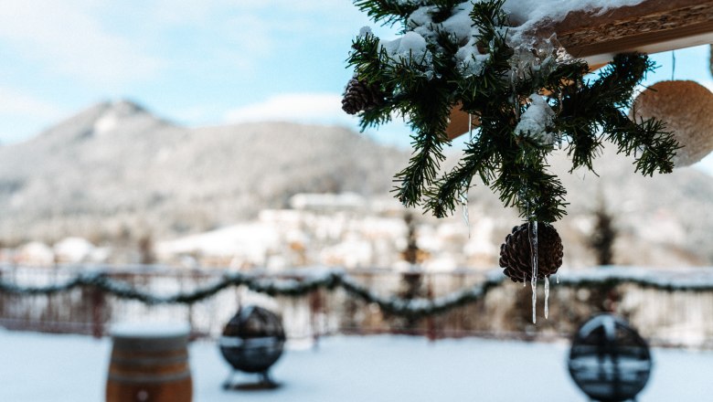 Die Terrasse im Winter, © Sporthotel Semmering Winterliche Terrasse mit Tannenzweigen und Eiszapfen im Vordergrund, schneebedeckte Landschaft im Hintergrund.