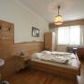 Berglandzimmer 1.Stock, © Scharfgger´s Raxalpen Resort Gemütliches Hotelzimmer mit Holzmöbeln, Doppelbett, Waschbecken und Fenster mit Vorhängen.