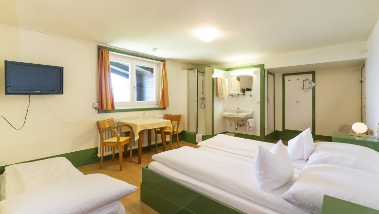 Looshaus, © Christian Redtenbacher Ein einfach eingerichtetes Hotelzimmer mit Doppelbett, Tisch, Stühlen, Fernseher und Waschbereich.