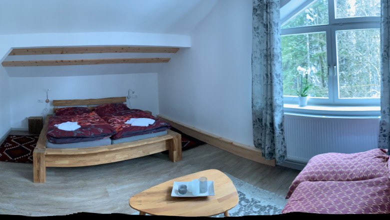 Schlafzimmer, © Seidl Gemütliches Schlafzimmer mit Holzbett, Sofa und großem Fenster mit Vorhängen.