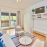 Top 2 - Wohnzimmer, © VP FeWo OG Modernes Wohnzimmer mit Sofa, Sessel, Glastisch und TV. Balkon mit Holzzaun im Hintergrund.