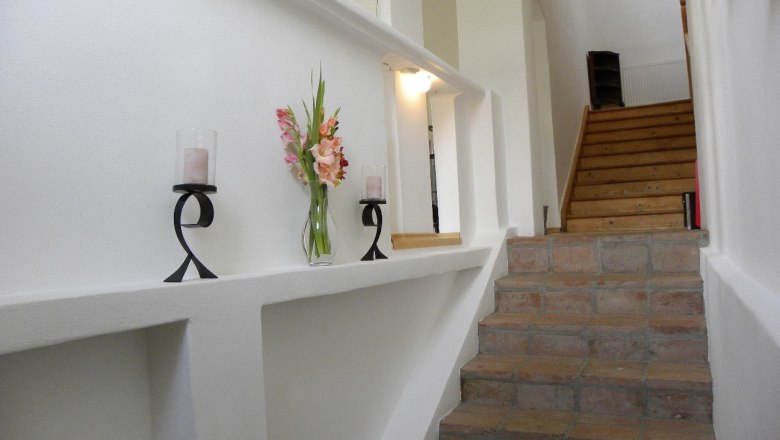 Details (Stiegenaufgang), © Thomas Baldauf Innenansicht eines Treppenaufgangs mit Kerzenhaltern und Blumen auf einem Sims.