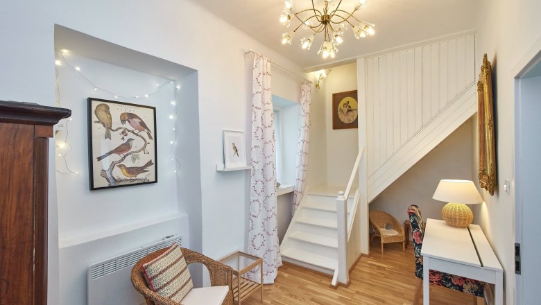 Top 4 - Wohnbereich, © VP FeWo OG Wohnbereich mit Treppe, Rattanmöbeln und Vogelbildern an der Wand.