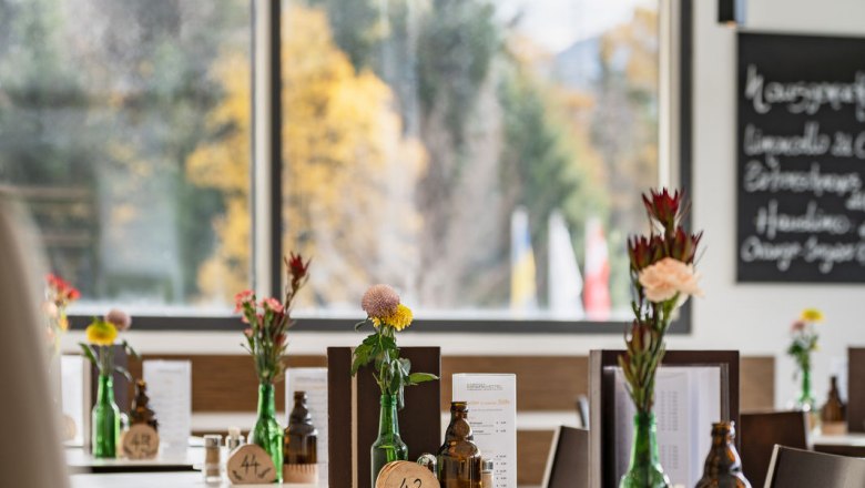 Bistro, © Kristina Polleres Innenansicht eines modernen Bistros mit Tischen, Blumenvasen und Menütafeln.