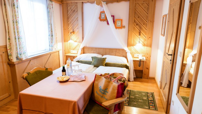 Doppelzimmer Kat. A, © Scharfegger´s Raxalpen Resort Gemütliches Doppelzimmer mit Holzmöbeln, einem Tisch mit Getränken und Snacks, und einem Bett mit Baldachin.
