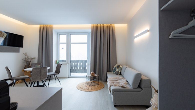 Apartment 4, © Atelier Fürtner-Ton Modernes Wohnzimmer mit grauem Sofa, Esstisch und Balkon.