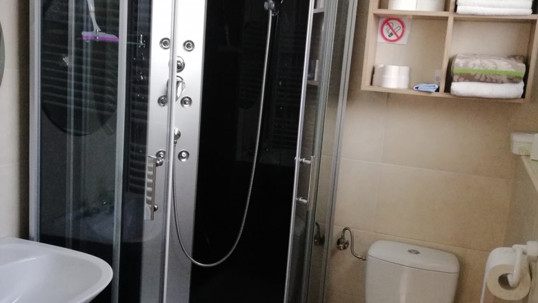 Badezimmer, © Kesper Modernes Badezimmer mit Duschkabine, Waschbecken, Toilette und Regal mit Handtüchern und Toilettenpapier.