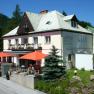 Der Löffler, © Sonja Löffler Ein zweistöckiges Gebäude mit der Aufschrift 'Löffler Pension-Café-Restaurant', umgeben von Bäumen und Blumen, mit orangenen Sonnenschirmen auf der Terrasse.
