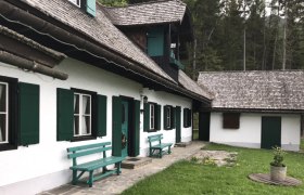 Ferienhaus Berghof Zifko, © Berghof Zifko Ein traditionelles Ferienhaus mit grünen Fensterläden und Holzbänken vor einem Wald.