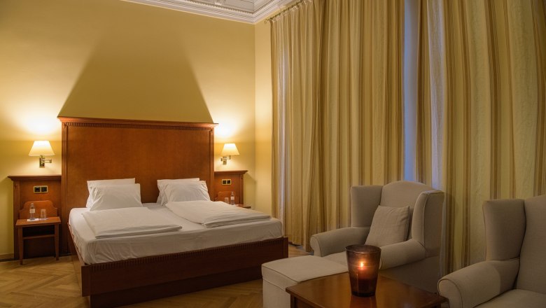 Doppelzimmer, © Traumbild - Gerhard Wolkersdorfer Elegantes Doppelzimmer mit großem Bett, zwei Sesseln und einem Tisch mit Kerze.