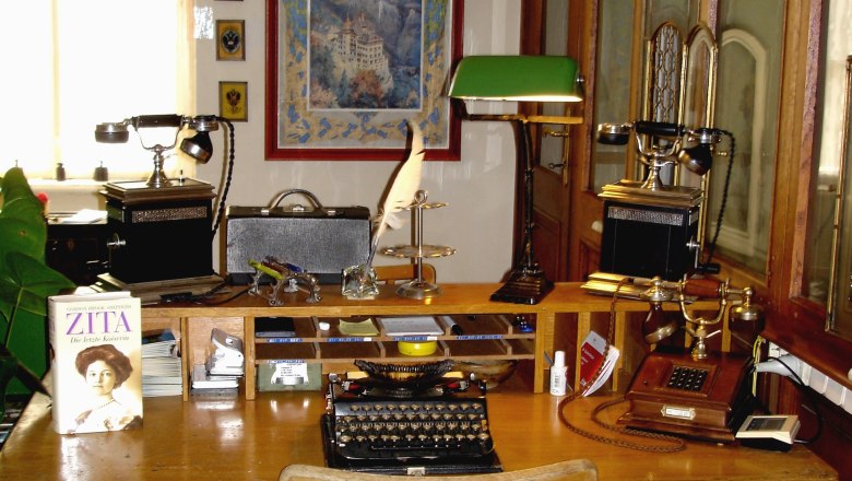 Schreibtisch Postamt Küb, © Marktgemeinde Payerbach Historischer Schreibtisch mit Schreibmaschine, Telefon und Büchern in einem Postamt.