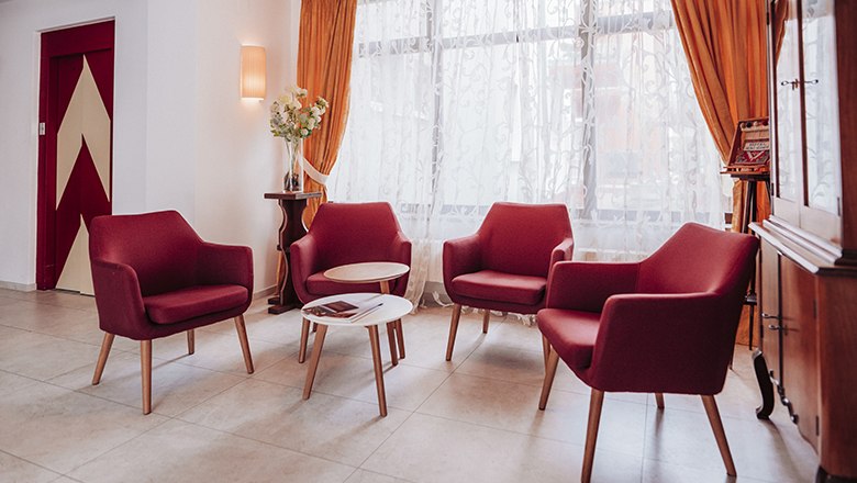 Payerbacherhof, © Payerbacherhof - Christopher Tarkus Gemütliche Sitzecke mit roten Sesseln und kleinem Tisch vor einem Fenster mit Vorhängen.