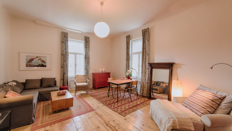 Top 3 - Wohnzimmer, © VP FeWo OG Gemütliches Wohnzimmer mit Holzboden, Sofa, Sessel, Esstisch und großem Spiegel.