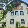 Ferienwohnungen Riedl, © Wiener Alpen Ein traditionelles Haus mit weißen Wänden, Holzfenstern und einem Balkon. Ein Baum und Pflanzen im Vordergrund.