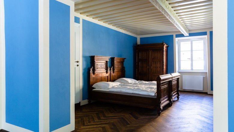 Zimmer, © Thalhof, Katrin Nusterer Ein Zimmer mit blauen Wänden, einem Holzbett und einem Schrank.