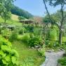 Ferienwohnungen Riedl, © Wiener Alpen Ein gepflegter Garten mit Blumen, Bäumen und einem Kiesweg, umgeben von einem Holzzaun und einer grünen Landschaft im Hintergrund.