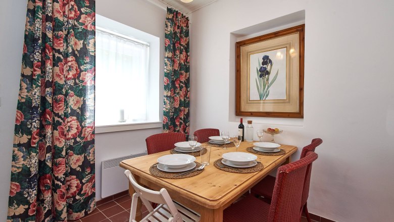 Top 4 - Esstisch, © VP FeWo OG Ein Esstisch mit vier Gedecken, roten Stühlen und einem Blumenbild an der Wand.