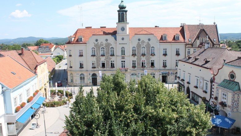 Rathaus am Hauptplatz, © Stadtgemeinde Neunkirchen Historisches Rathaus an einem sonnigen Hauptplatz mit umliegenden Gebäuden und Bäumen.