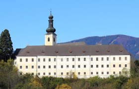 Schloss Gloggnitz, © BWAG Schloss Gloggnitz vor bewaldeten Hügeln und blauem Himmel.