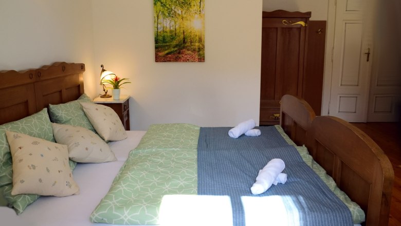 Doppelzimmer, © Reinhard Maurer Gemütliches Doppelzimmer mit Holzmöbeln, grünem Bettzeug und einem Bild an der Wand.