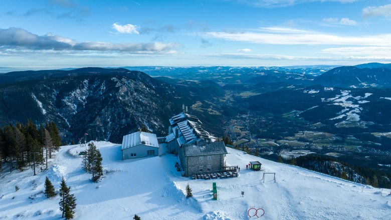 Drohnenbilder Raxalm-Berggasthof, © KS Content & Marketing Luftaufnahme des Raxalm-Berggasthofs im Winter mit schneebedeckten Bergen und Tälern im Hintergrund.