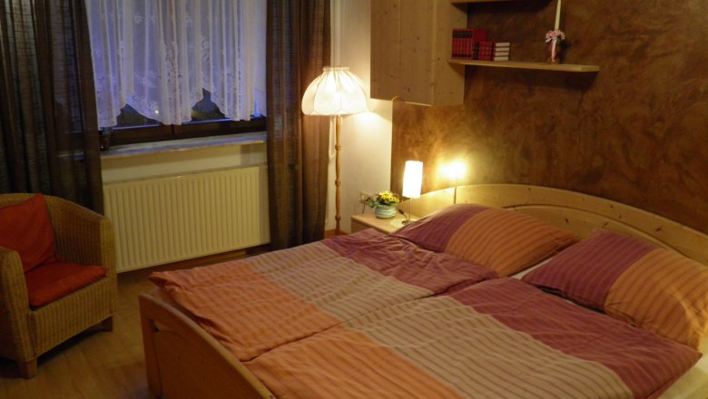 Schlafzimmer, © Kesper Gemütliches Schlafzimmer mit Doppelbett, Nachttischlampen, Bücherregal und Sessel.