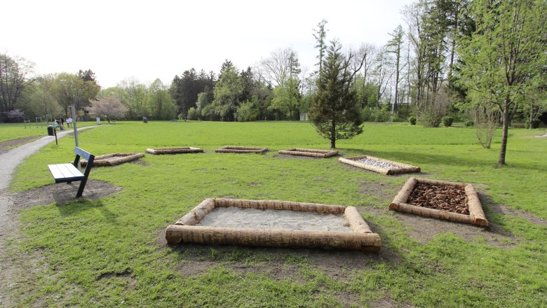 Stadtpark Neunkirchen, © Stadtgemeinde Neunkirchen Ein Stadtpark mit einem Barfußpfad aus verschiedenen Materialien und einer Parkbank.