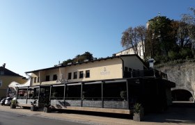 Bevanda, © Wiener Alpen Gebäude mit der Aufschrift 'Bevanda' und Terrasse, umgeben von Bäumen und Felsen.