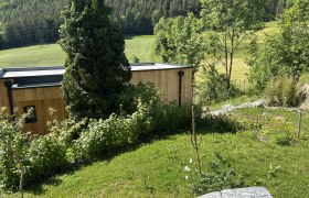 Hausansicht, © Stupacher Holzhaus in grüner Landschaft mit Bäumen und Wiese.