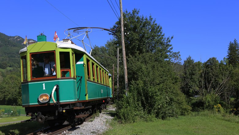 Höllentalbahn, © ÖGLB/Albert Malli Historische grüne Bahn fährt durch eine grüne Landschaft unter blauem Himmel.