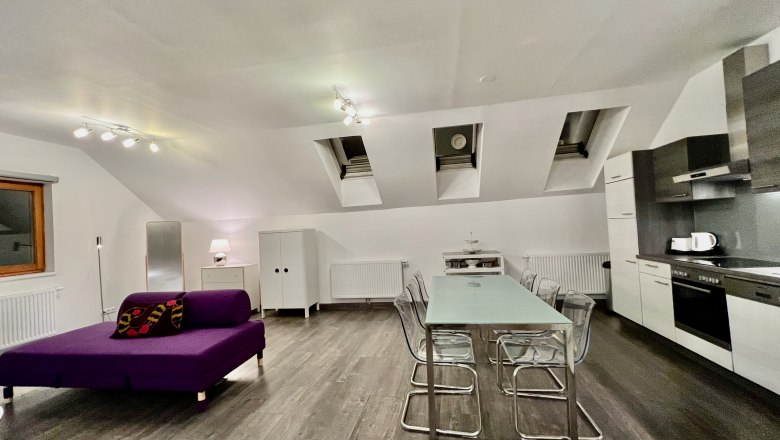 Loft am Hauptplatz, © Relax Apartments Modernes Loft mit offener Küche, Esstisch und lila Sofa.