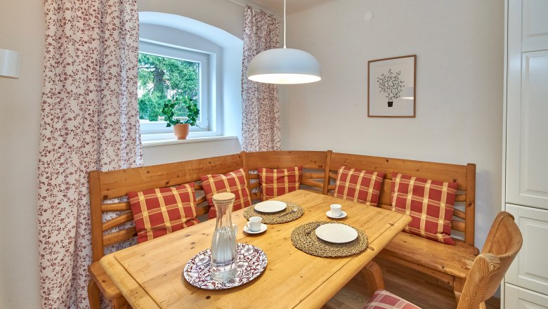 Top 3 - Essbereich, © VP FeWo OG Gemütlicher Essbereich mit Holztisch, Eckbank und karierten Kissen.