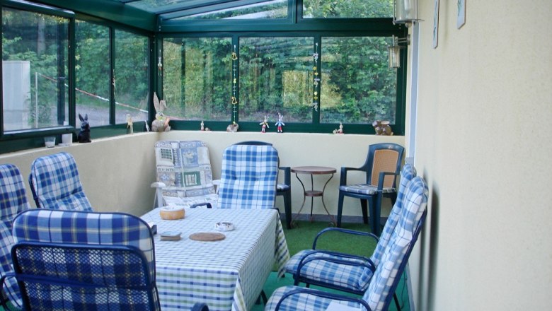 Wintergarten Ferienhaus Anna, © Vadim Drozdov Wintergarten mit Tisch und Stühlen, dekoriert mit Figuren.