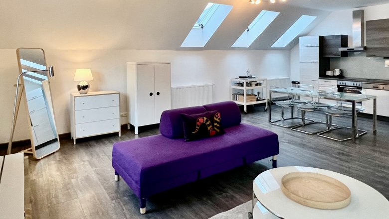 Loft am Hauptplatz, © Relax Apartments Modernes Loft mit violettem Sofa, Esstisch und Küche unter Dachfenstern.