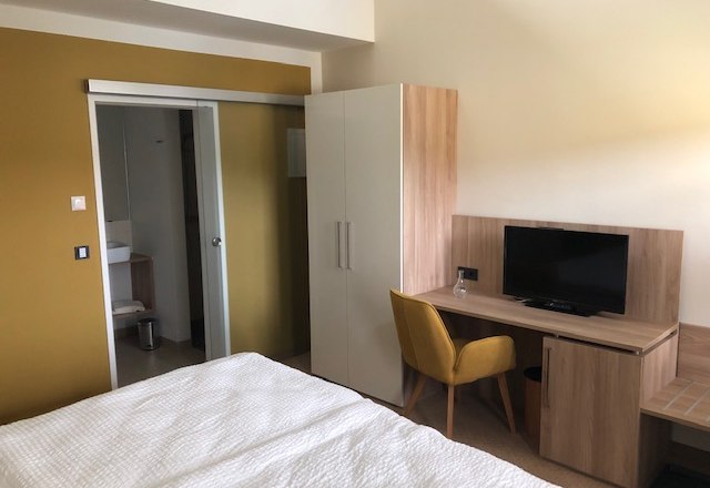 Gästezimmer, © Alexandra Heiling-Niegl Ein modernes Gästezimmer mit Bett, Schreibtisch, Stuhl, Fernseher und Schrank. Im Hintergrund ist ein Badezimmer zu sehen.