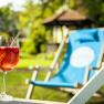 Sommerfrische pur, © Wiener Alpen/Martin Fülöp Ein Glas mit rotem Getränk und Strohhalm auf einem Liegestuhl im Garten.
