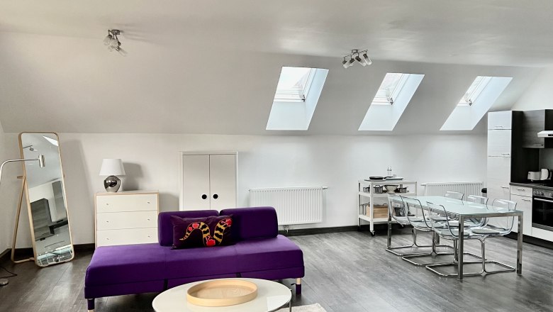 Loft am Hauptplatz, © Relax Apartments Modernes Loft mit violetten Sofas, Esstisch und Küchenzeile unter Dachfenstern.